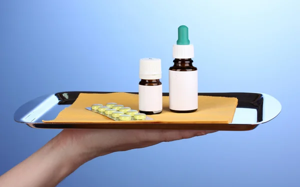 Ruka drží tác s léky na modrém pozadí — Stock fotografie