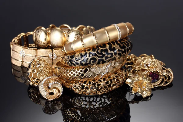 Schöne goldene Armbänder, Ringe und Schmuck auf grauem Hintergrund — Stockfoto