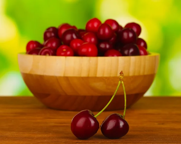 Cherry in wooden bowl on wooden table on green background — Stock Photo, Image