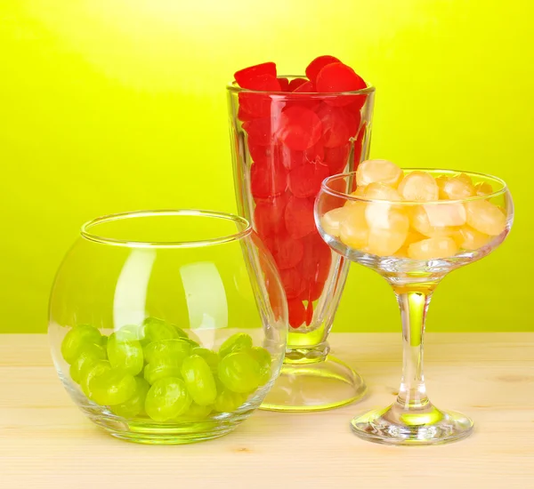 Color candies in glasses on wooden table on green background — Stock Photo, Image