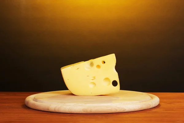 Stock image Cheese on cutting board on wooden table on brown background