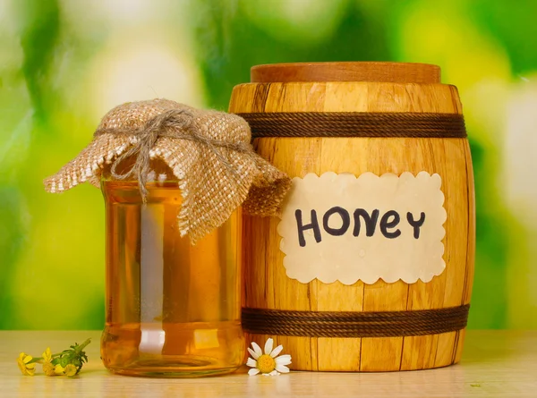 Dolce miele in botte e vaso con fiori su tavolo di legno su sfondo verde — Foto Stock