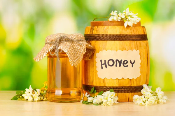 Zoete honing in vat en pot met bloemen op houten tafel op groene achtergrond — Stockfoto