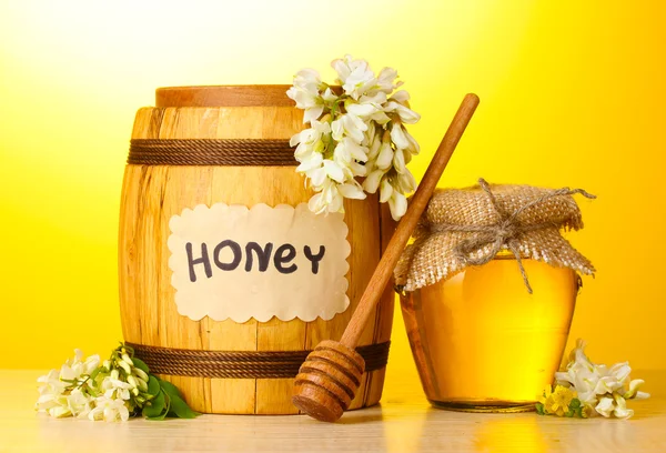 バレルとアカシアの花の黄色の背景に木製のテーブルの上の瓶に甘い蜂蜜 — ストック写真