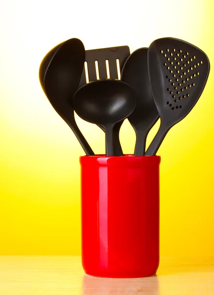 Utensilios de cocina negro en taza roja sobre fondo amarillo — Foto de Stock