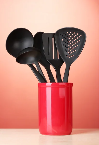 Black kitchen utensils in cup on red bakground — Stock Photo, Image