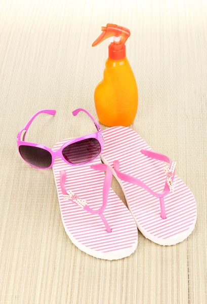 Vaaleanpunaiset rantatohvelit aurinkolaseilla ja aurinkovoiteella matolla — kuvapankkivalokuva