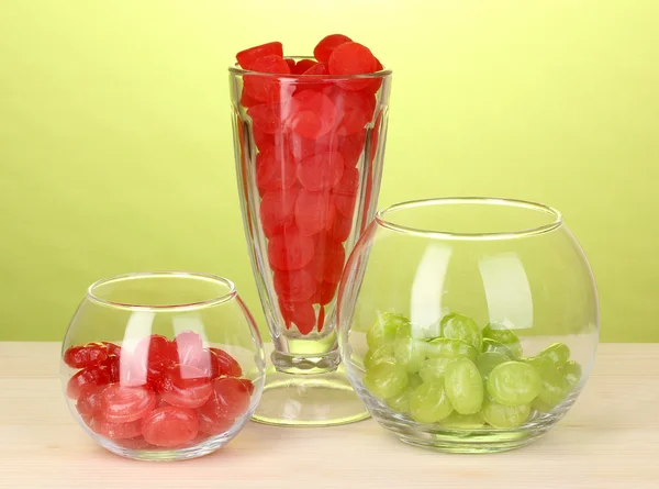 Цветные конфеты в стаканах на деревянном столе на зеленом фоне — стоковое фото