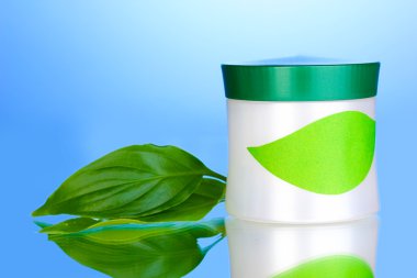 Jar of cream with green leaves on blue background clipart