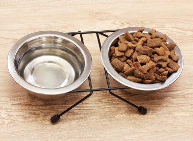 Dry dog food and water in metal bowls on wooden background clipart