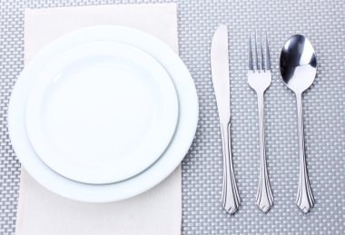 White empty plates with fork, spoon and knife on a grey tablecloth