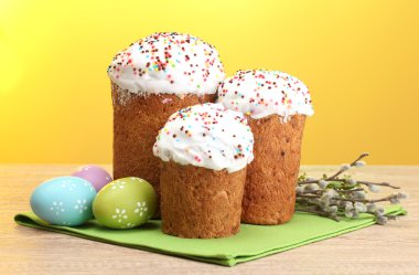 Beautiful Easter cakes, colorful eggs and pussy-willow twigs on wooden table on yellow background clipart