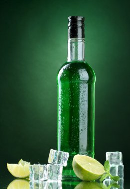 şişe absinthe yeşil zemin üzerine buz ve limon ile