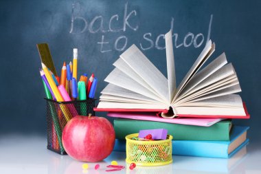 Composition of books, stationery and an apple on the teacher's desk in the background of the blackboard. Back to school. clipart