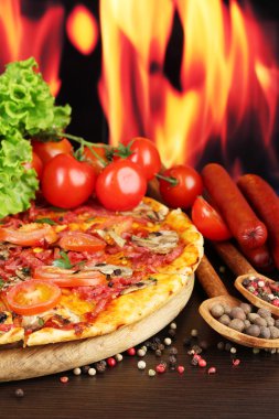 güzel pizza, salam, domates ve baharatlar alev arka plan üzerinde ahşap tablo