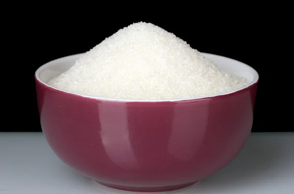 Eine bunte Schüssel voller weißer Zucker auf schwarzem Hintergrund — Stockfoto