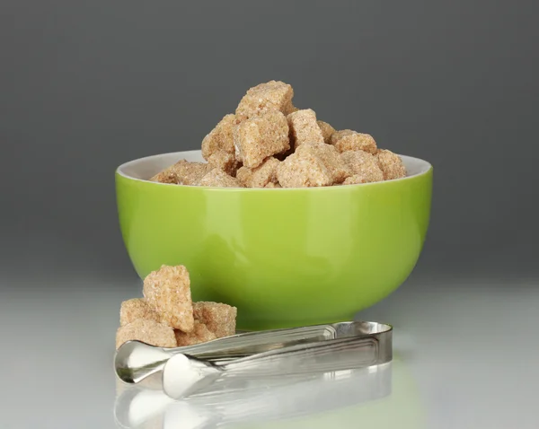 Brunt rörsocker kuber i skålen med socker-tång på grå bakgrund — Stockfoto