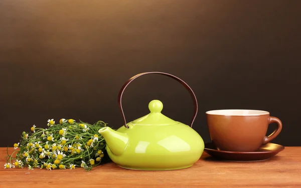 Teapot and cup with chamomile tea on wooden table on brown background — Stock Photo, Image