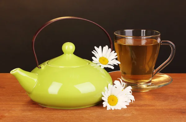 Чайник и чашка с ромашковым чаем на деревянном столе на коричневом фоне — стоковое фото