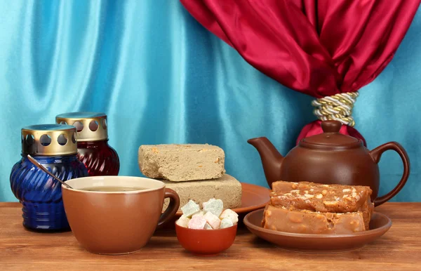 Bule com xícara e pires com doces orientais - sherbet, halva e prazer turco em mesa de madeira em um fundo de close-up cortina — Fotografia de Stock