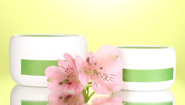 緑色の背景で花とクリームの瓶 — ストック写真