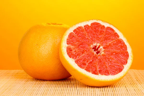 Rijp grapefruit en de helft op bamboe mat op gele achtergrond — Stockfoto