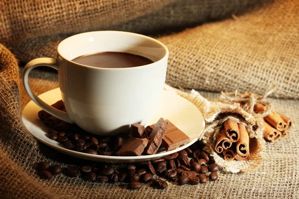 Cup of coffee and beans, cinnamon sticks and chocolate on sacking background — Stock Photo, Image