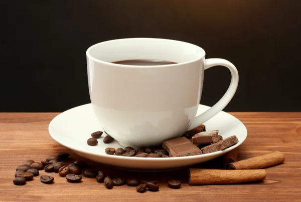 Чашка кофе и бобов, коричные палочки и шоколад на деревянном столе на коричневом фоне — стоковое фото