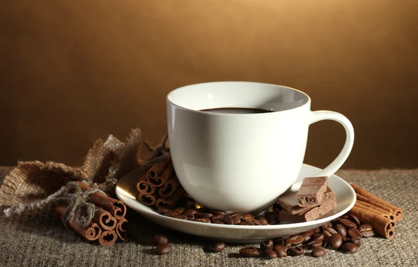 Xícara de café e feijão, paus de canela e chocolate no saque no fundo marrom — Fotografia de Stock