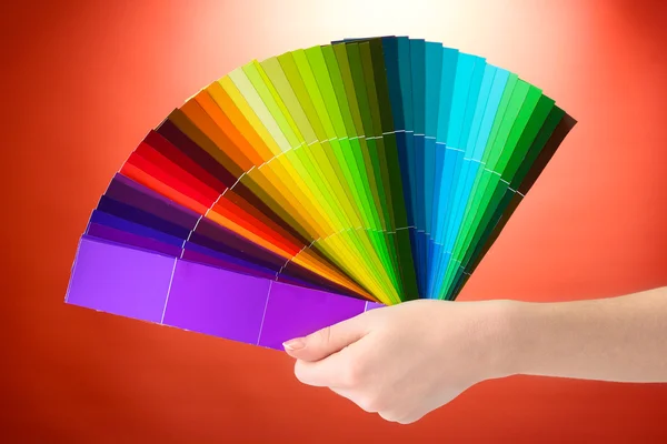 Mão segurando paleta brilhante de cores no fundo vermelho — Fotografia de Stock