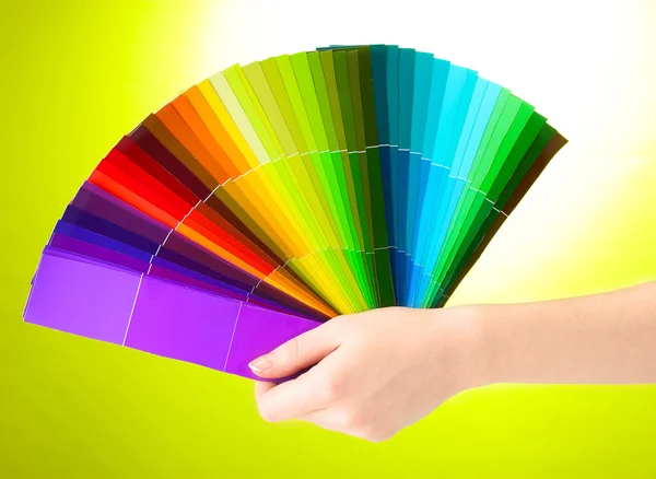 Mão segurando paleta brilhante de cores no fundo verde — Fotografia de Stock