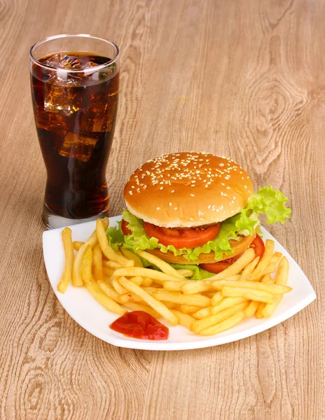 Big and tasty hamburger and fried potatoes on plate with cola on wooden table — Stock Photo, Image