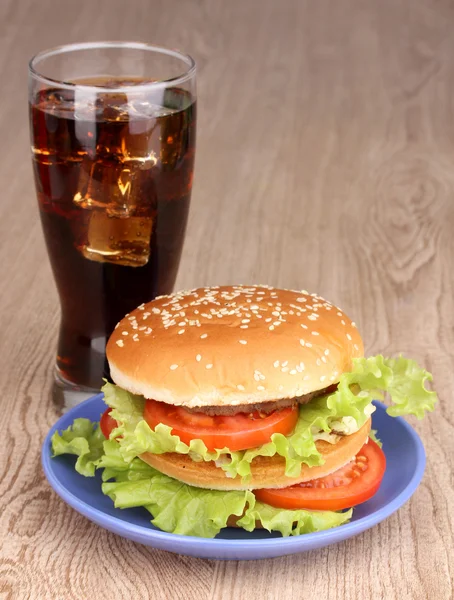 Hambúrguer grande e saboroso na chapa com cola na mesa de madeira — Fotografia de Stock