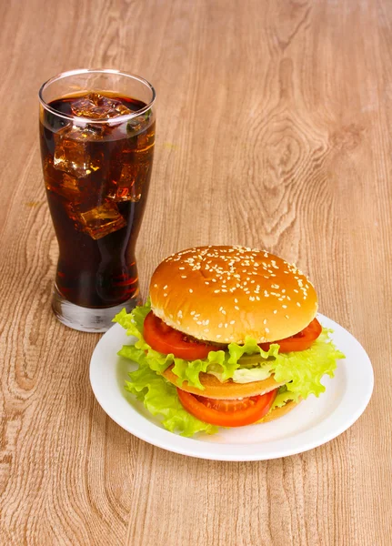 Großer und schmackhafter Hamburger auf Teller mit Cola auf Holztisch — Stockfoto