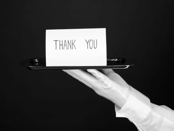Ruku v rukavici, držící stříbrný podnos s kartou poděkovat izolované na černém — Stock fotografie
