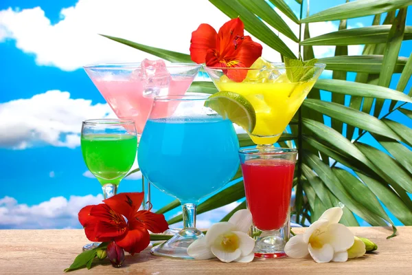 Екзотичні коктейлі та квіти на столі на фоні блакитного неба — стокове фото