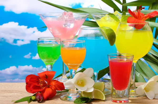 Exotische Cocktails und Blumen auf dem Tisch vor blauem Himmel Hintergrund — Stockfoto