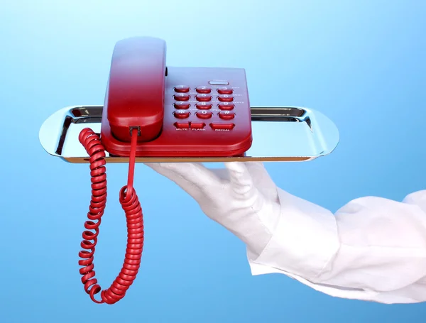 Hand in glove holding silver tray with telephone on blue background — Stock Photo, Image