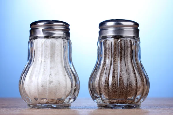 Sól i pieprz mills na drewnianym stole na niebieskim tle — Zdjęcie stockowe