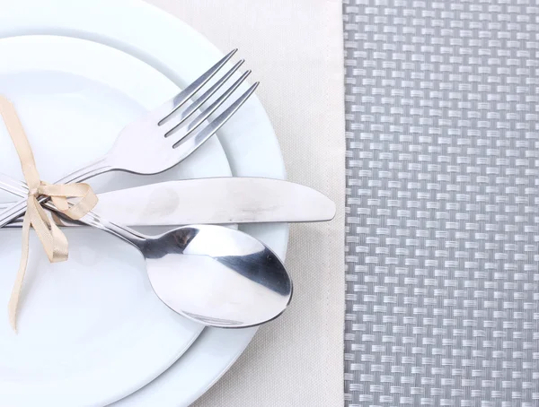 Assiettes blanches vides avec fourchette, cuillère et couteau attachées avec un ruban sur une nappe grise — Photo