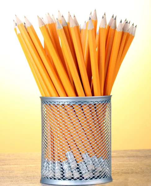 Ołówków w metalowy kubek na drewnianym stole na żółtym tle — Zdjęcie stockowe