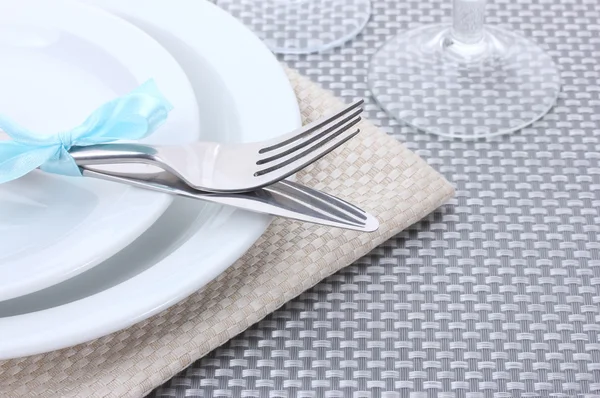 Bílé prázdné talíře, vidličku a nůž převázaná stuhou a brýle na šedé ubrus — Stock fotografie