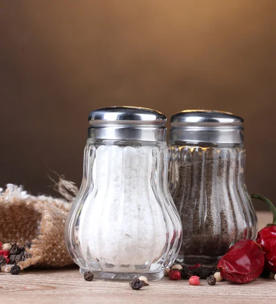 Sůl a pepř mlýny a koření na dřevěný stůl na hnědé pozadí — Stock fotografie
