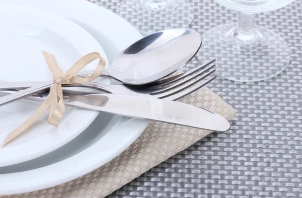 Białe puste talerze, widelec i nóż związany ze wstążki i okulary na szary Obrus — Zdjęcie stockowe