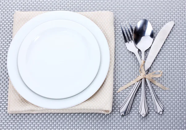 Bílé prázdné talíře, vidličku, lžíci a nůž svázané stuhou na šedé ubrus — Stock fotografie