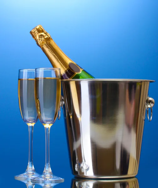 Bottiglia di champagne in secchio con ghiaccio e bicchieri di champagne, su sfondo blu — Foto Stock