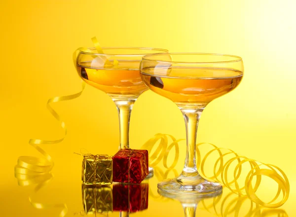 Glasses of champagne, gifts and streamer on yellow background — Stock Photo, Image