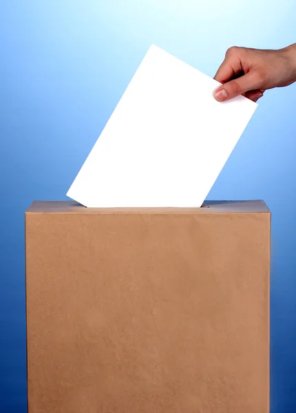 Mão com cédula de voto e caixa no fundo azul — Fotografia de Stock