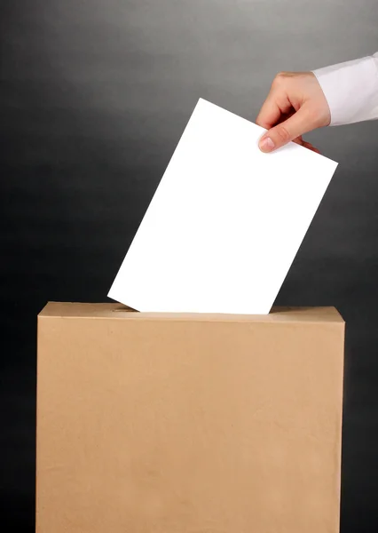 Mano con papeleta de votación y caja sobre fondo gris — Foto de Stock