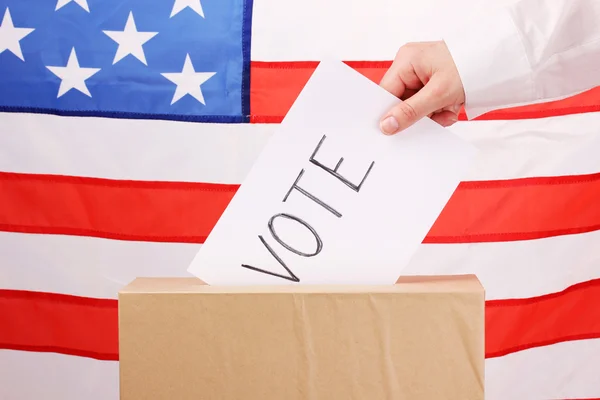 Mano con papeleta de votación y caja en Bandera de Estados Unidos — Foto de Stock